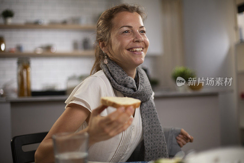 快乐的年轻女人在家里吃三明治。