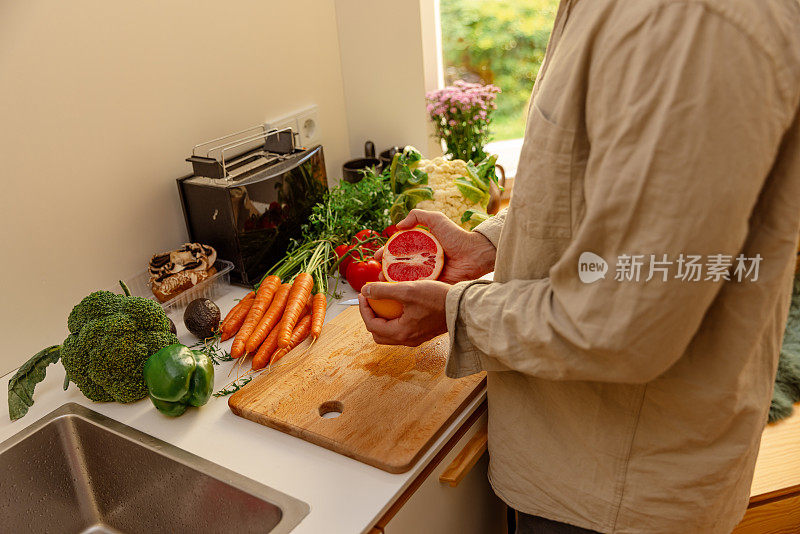 在厨房里，年轻人的手拿着半个红葡萄柚——准备生素食食谱——特写镜头