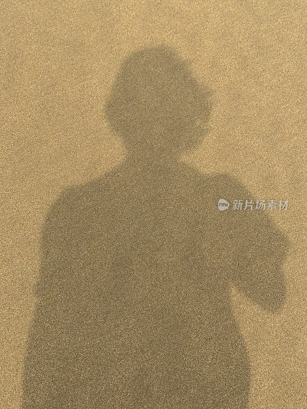 在强烈的阳光下，无法辨认的人的影子投射在金色的沙滩上的特写图像，阳光下的人的轮廓，剪影，高架视图