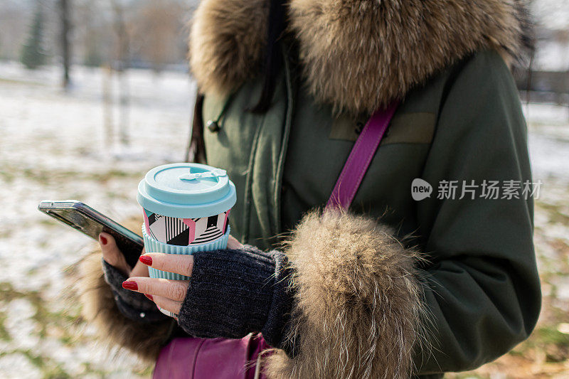 在一个下雪的冬日，一位美丽的年轻女子在公园里享受着她的咖啡。她在自拍，或者视频通话。