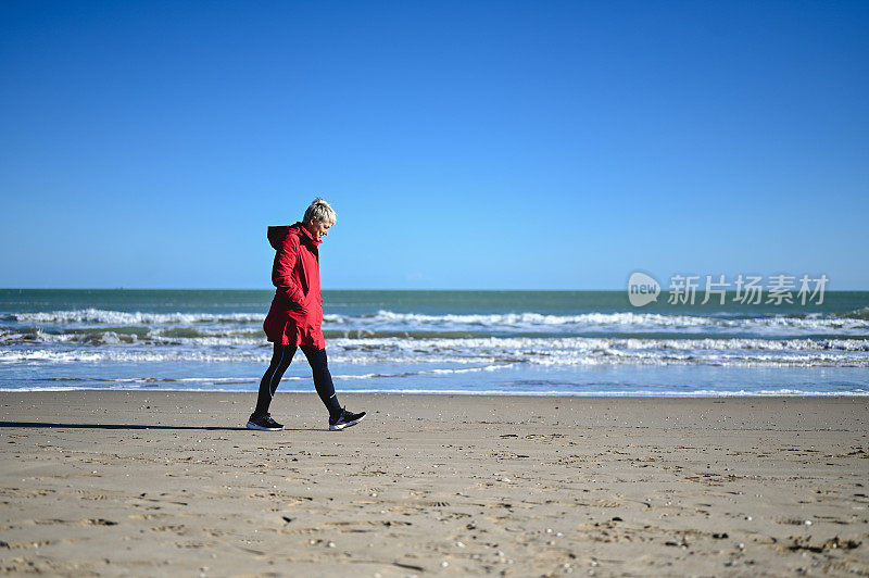 一位老妇人在空旷的沙滩上走过沙丘。