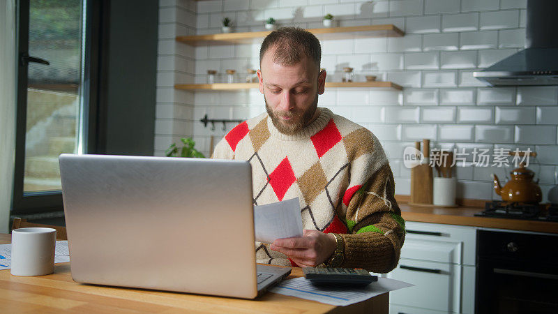 成年男人坐在厨房用平板电脑支付账单，用计算器计算费用，做预算控制，管理财务，审查逾期贷款