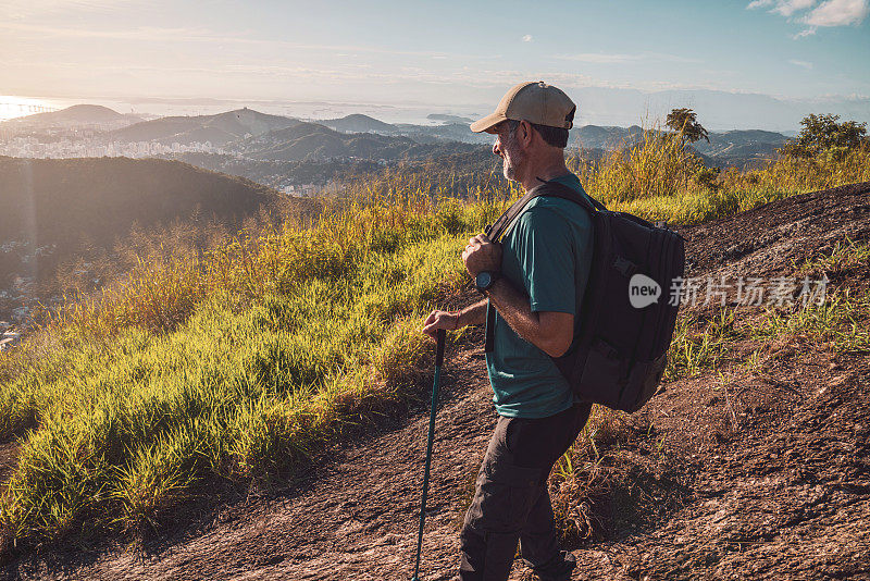 一个男人站在山顶上，拄着一根登山杖，享受着他在山上的冒险