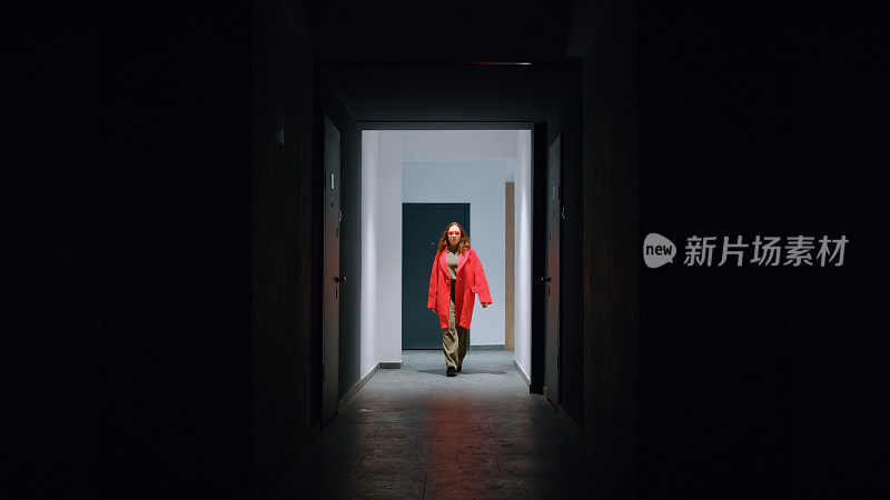 穿红衣服的女人走在一座居民楼的照明走廊上