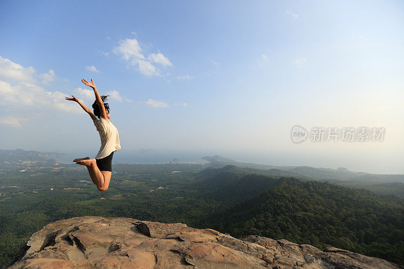 欢呼年轻的亚洲女子跳上山峰岩石
