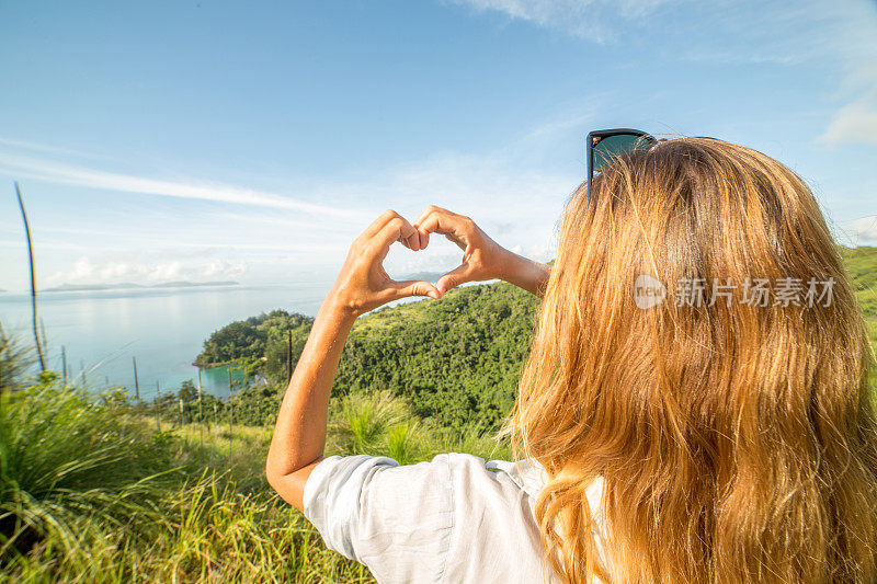 一位年轻女子为海景制作心形手指架