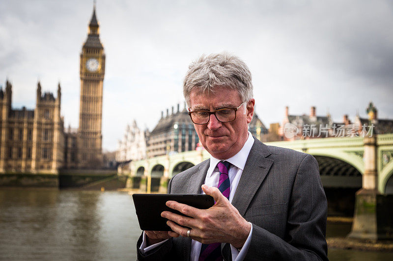 英国伦敦，一位资深商人看着他的数字平板电脑，背景是大本钟和议会