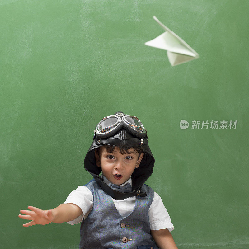 带着飞行眼镜的小男孩在黑板前扔纸飞机