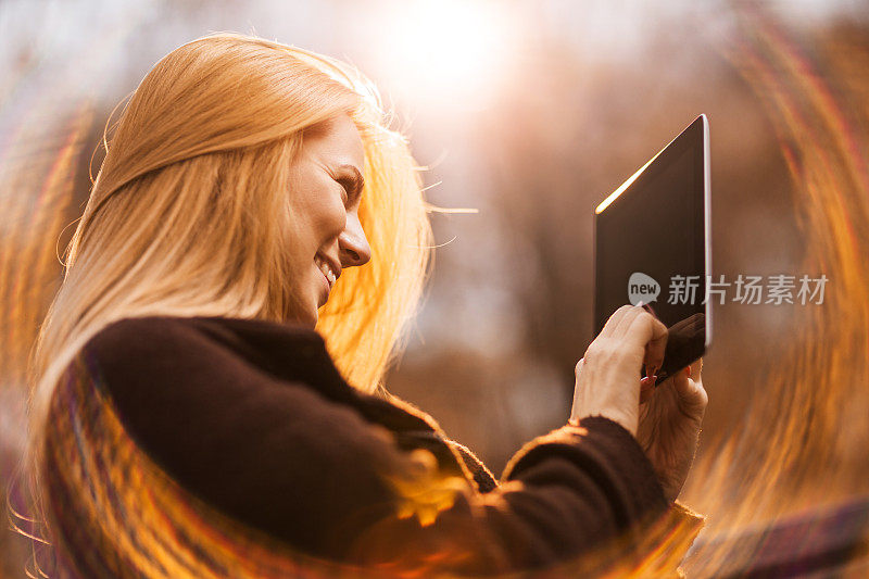一个微笑的女人在户外使用触控板的侧视图。