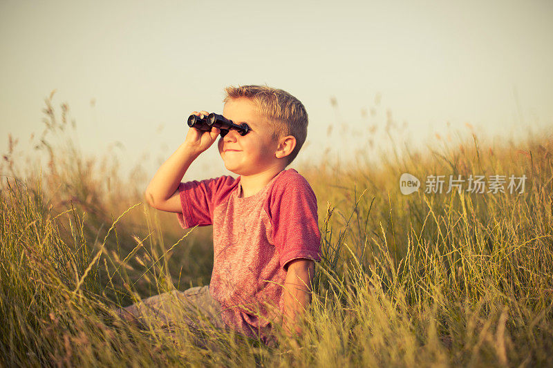 坐在草地上看望远镜的小男孩