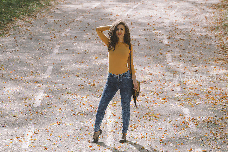 美丽的微笑卷曲的女孩在街头摆姿势的秋天