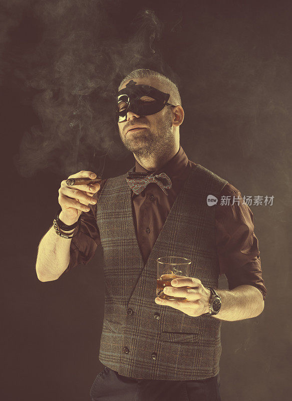优雅的男人戴着狂欢节面具，喝着威士忌，抽着雪茄