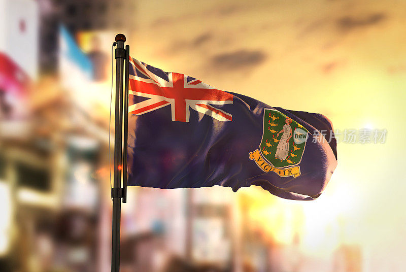 在日出的背光下，英属维尔京群岛的旗帜对着城市模糊的背景