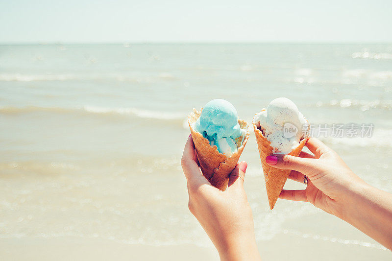 女人的手拿着两个冰淇淋在海上的背景。夏天。假期。