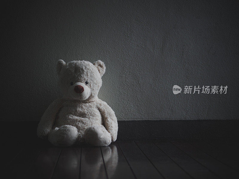 孤独的泰迪熊坐在黑暗的房间里(爱的概念)