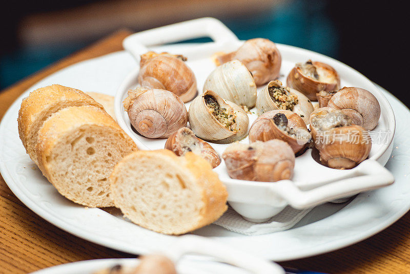 蜗牛配香草黄油，在传统的陶瓷平底锅里，面包和酱汁放在质朴的木桌上。俯视图
