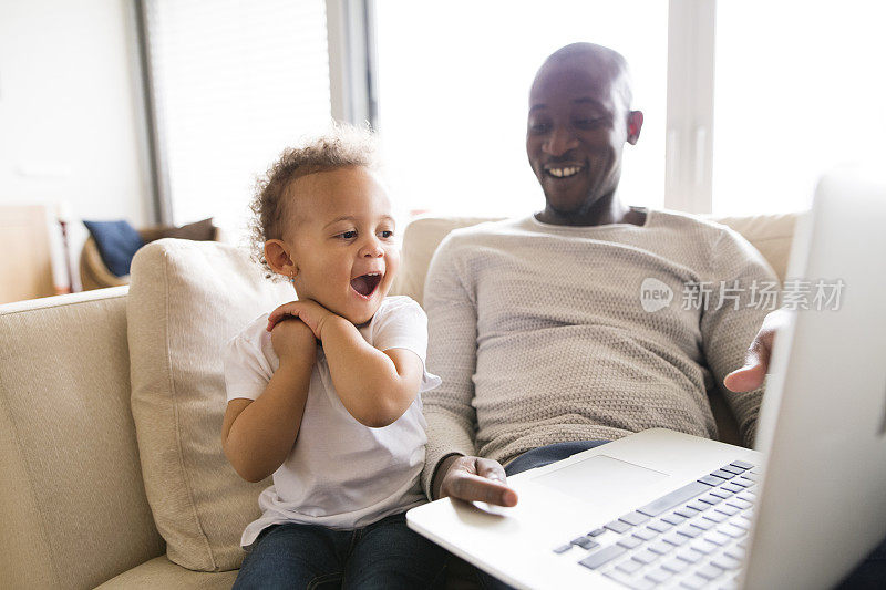 非裔美国父亲和小女儿在家拿着笔记本电脑。