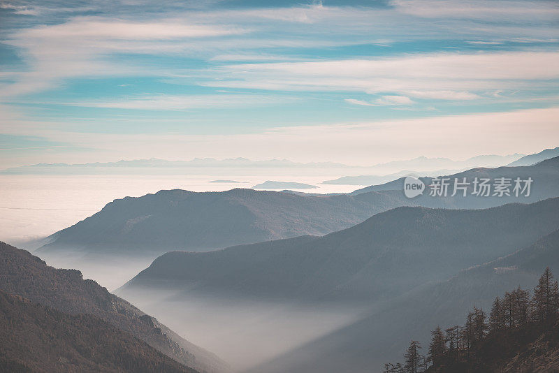 远处的山脉覆盖着雾气和薄雾下面的山谷。意大利阿尔卑斯山，色调形象。