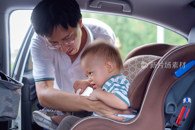 亚洲父亲帮助他可爱的1岁的亚洲小男孩系安全带在汽车安全座椅上