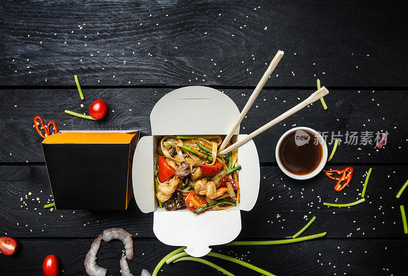 锅。乌冬炒面与海鲜在一个盒子黑色的背景。用筷子和酱汁。