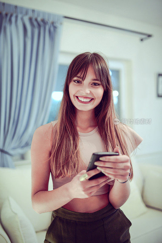 年轻微笑的女性在家里使用手机