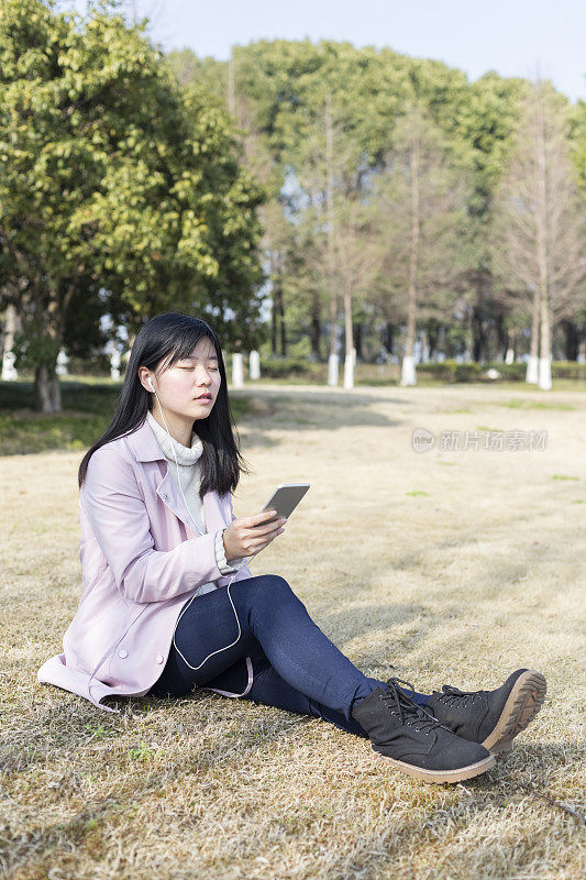 一个春天的下午，年轻女子戴着耳机在草坪上放松