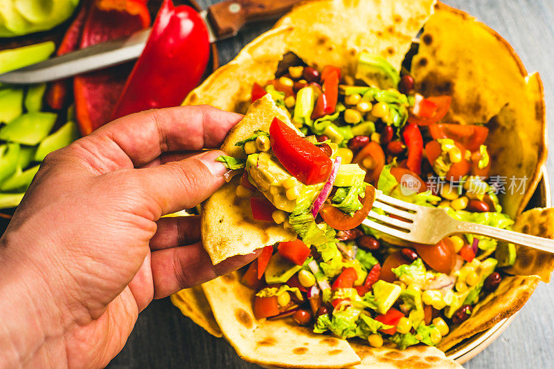 经典的墨西哥玉米沙拉，鳄梨、玉米、辣椒、番茄、豆类和玉米饼片——一个男人的手与沙拉