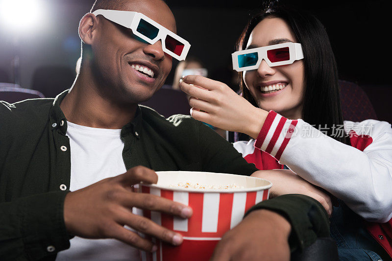 戴着3d眼镜的异族情侣在电影院边看电影边吃爆米花