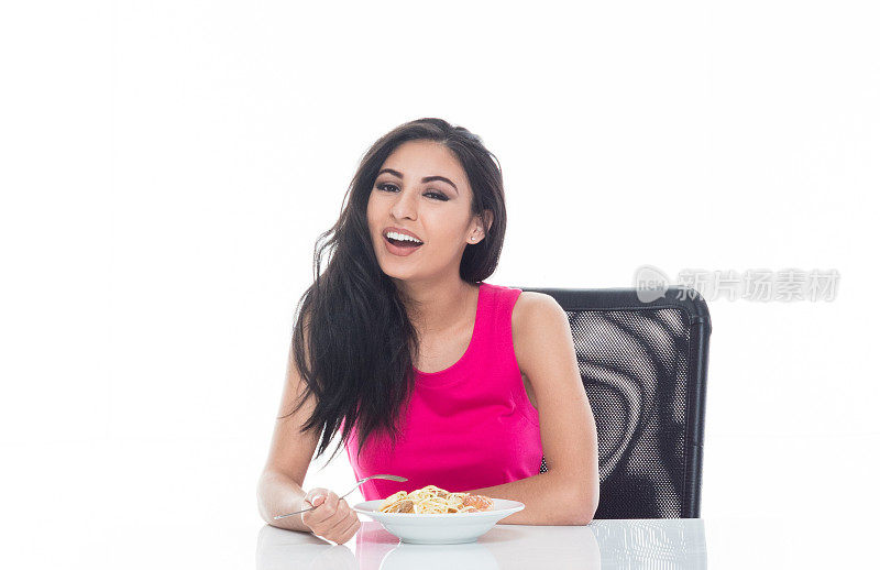 美丽的拉丁女性坐在一个白色的桌子上吃她的健康的意大利面午餐
