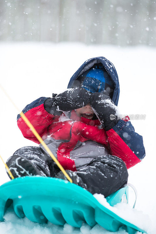 蹒跚学步的小男孩被小雪橇拉着穿过雪地