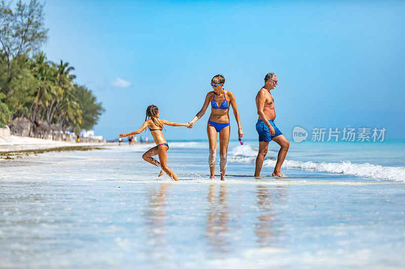一家人带着一个孩子在热带岛屿的海岸线上行走