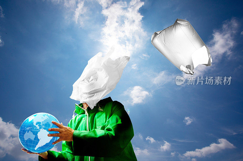 一个穿着绿色雨衣的渔民的脸上贴着一个塑料购物袋。一个超现实的微塑料环境污染和海洋污染的形象。