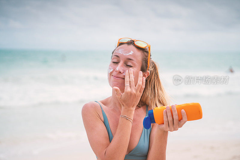 夏日——年轻女子在海滩上涂抹防晒霜，保护皮肤