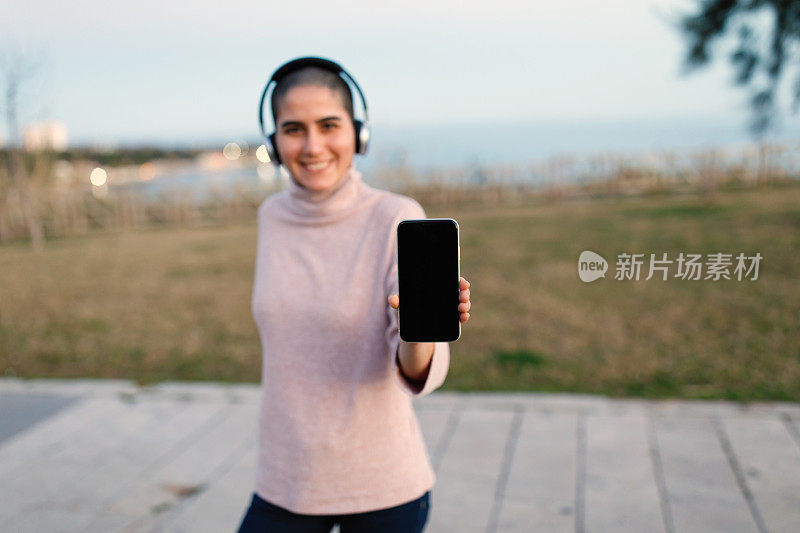 年轻女子在户外展示手机和听音乐