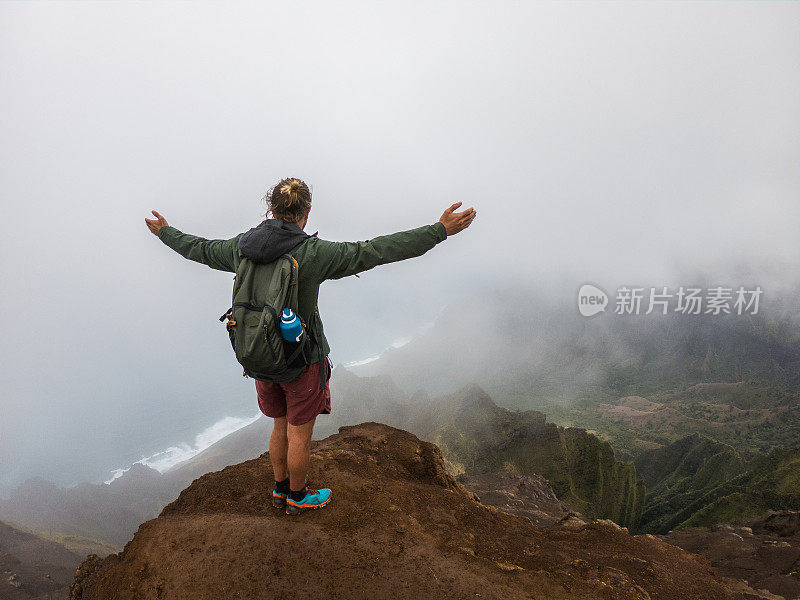 美国夏威夷，一个年轻人站在山顶，眺望着张开双臂的大海