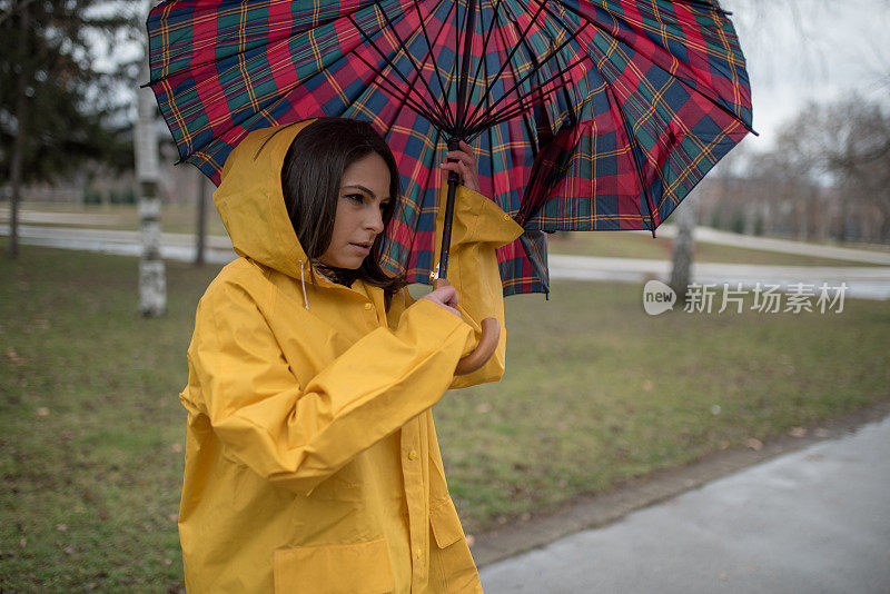 穿着黄色雨衣的年轻女子在公园里度过雨天