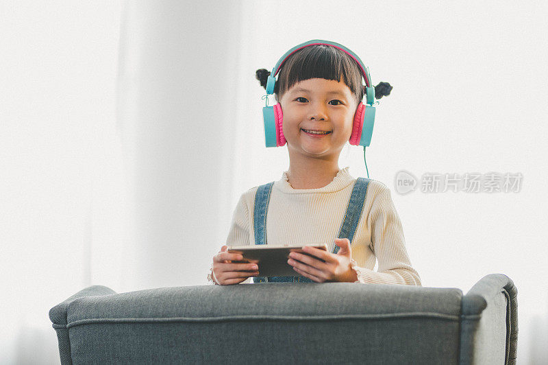 年轻的亚洲女孩坐在家里客厅的沙发上用智能手机玩游戏