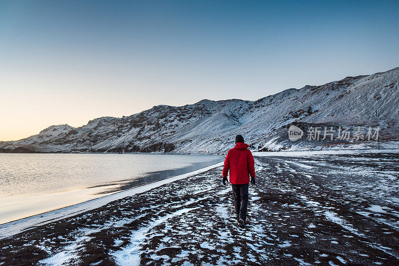 一名男性游客在冬季参观冰岛的克莱法瓦特湖，那里有令人惊叹的冰雪覆盖的山景