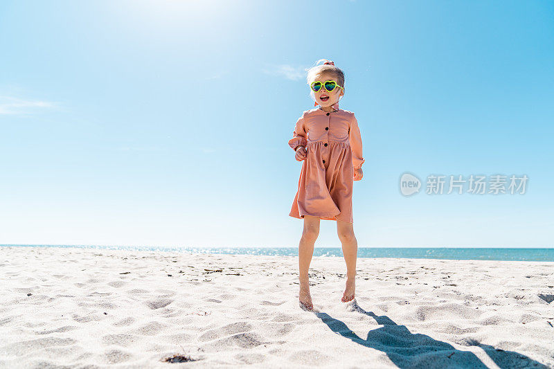 一个五岁的小女孩在一个晴朗无云的日子里在沙滩上奔跑跳跃。