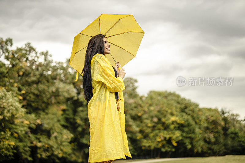 美丽的年轻女子穿着黄色雨衣，拿着黄色雨伞在户外