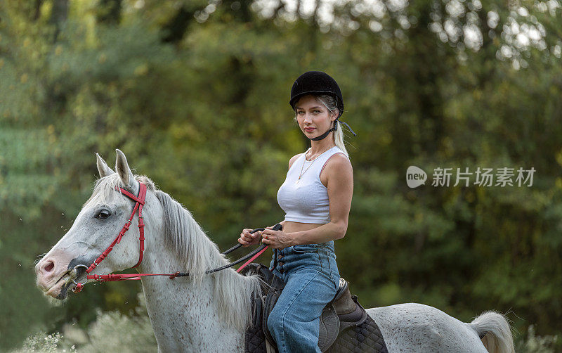 年轻美丽的女人和她的马在牧场自由漫步