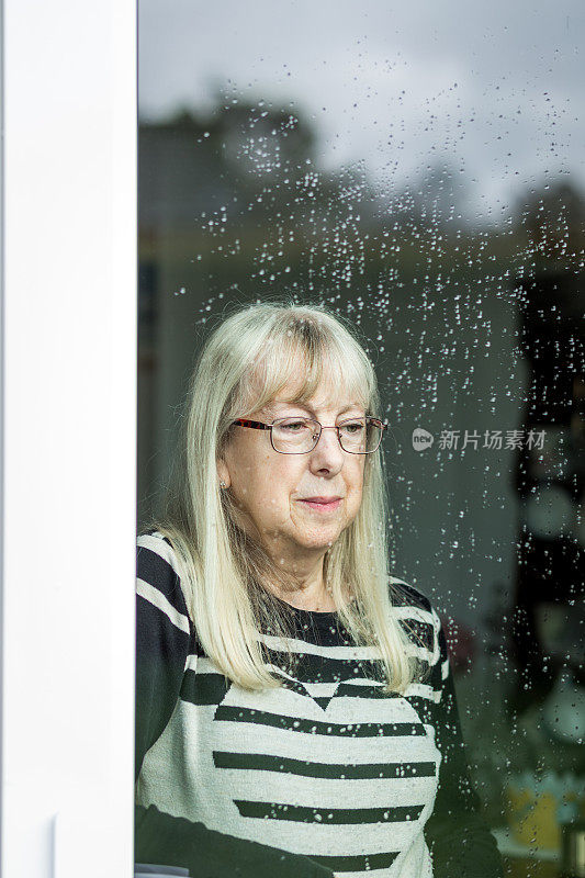 沮丧的资深妇女望着窗外的雨