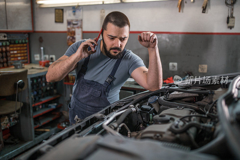 汽车修理工在汽车修理厂检查损坏车辆时使用手机