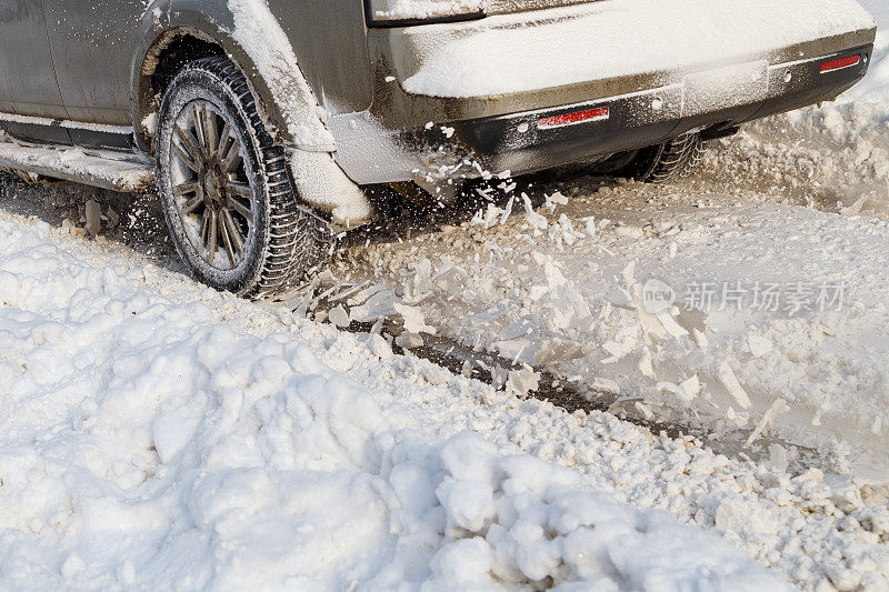 道路上的雪从车辆的纺车上飞起来。汽车的轮子旋转，吐出雪片，试图在湿滑的道路上获得牵引力。