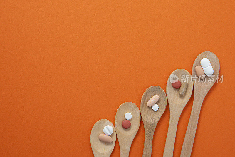 药丸的高角度视图，不同颜色的药物药丸与不同的甜汤匙在橙色的背景