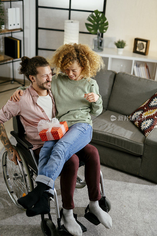 一个坐在轮椅上的年轻男子在家里用库存照片送给女友一个惊喜