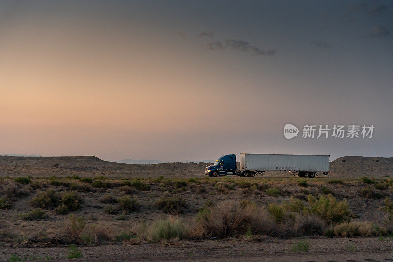 一辆商业货运半挂车正行驶在沙漠公路上，一个戏剧性的日落背景