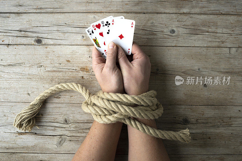 男人的手被绳子绑着，他的手里握着扑克牌，沉迷于概念，沉迷于赌博