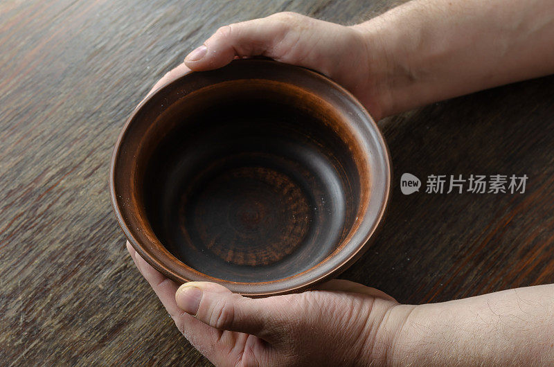 一只空碗，一个男人的手放在一张棕色的旧桌子上。