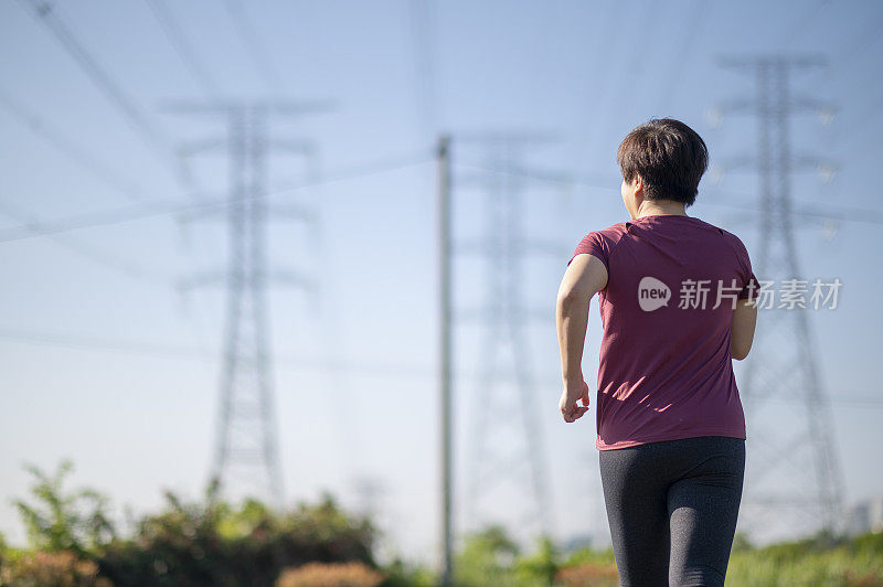 后视图亚洲华人中年妇女与运动服跑步在早上与电力线蓝色的天空背景